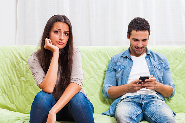 Couple sitting together while one partner is distracted by phone, illustrating phubbing in relationships