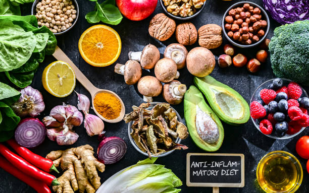 Colorful anti-inflammatory eating including salmon, berries, leafy greens, walnuts, and olive oil arranged on a wooden table